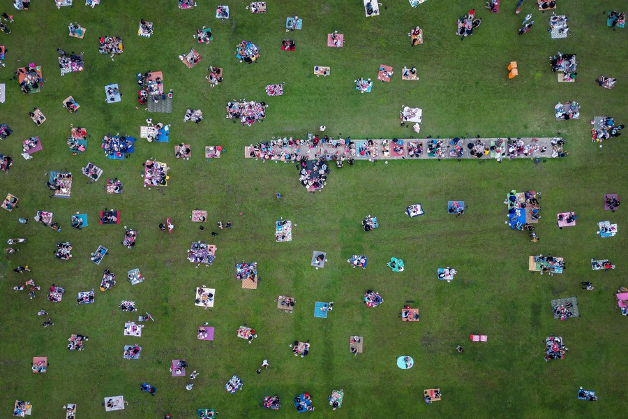An aerial view of people eating while sitting on blankets in a park
