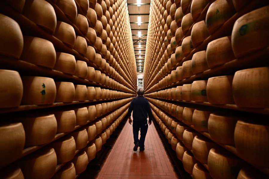 A worker walks by hundreds of stacked wheels of cheese.
