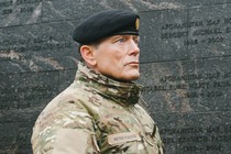 a color photograph of Denmark's military chief wearing fatigues and beret in front of a national war memorial