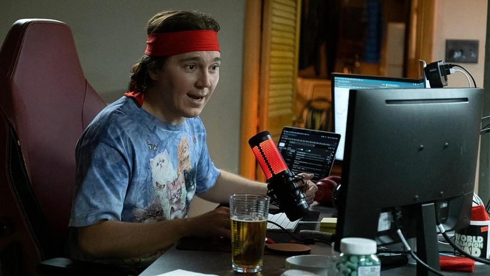 a man in a sweatband and cat tshirt sitting at desk speaking into a microphone