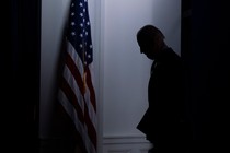 A dark photo of the silhouette of Joe Biden standing by an American flag