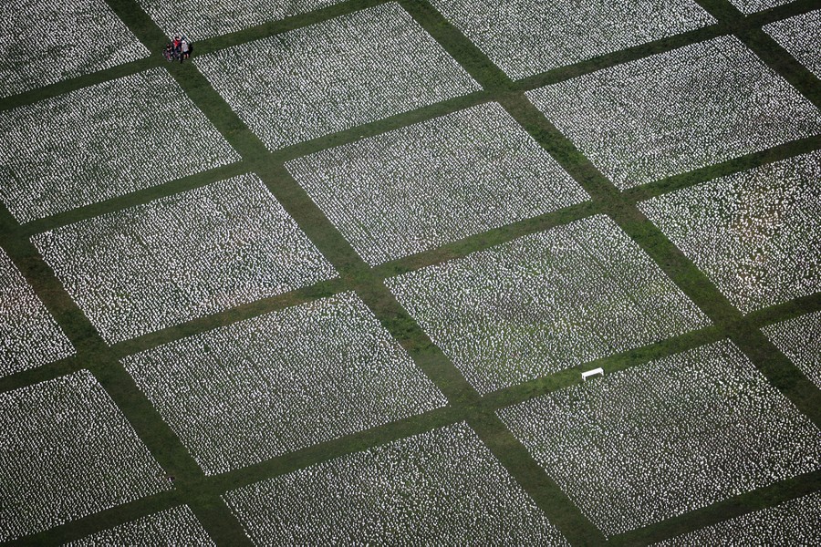 People walk through a large field of small white flags, seen from above.