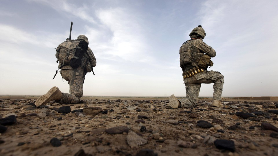 Two soldiers kneel on the ground in Afghanistan.