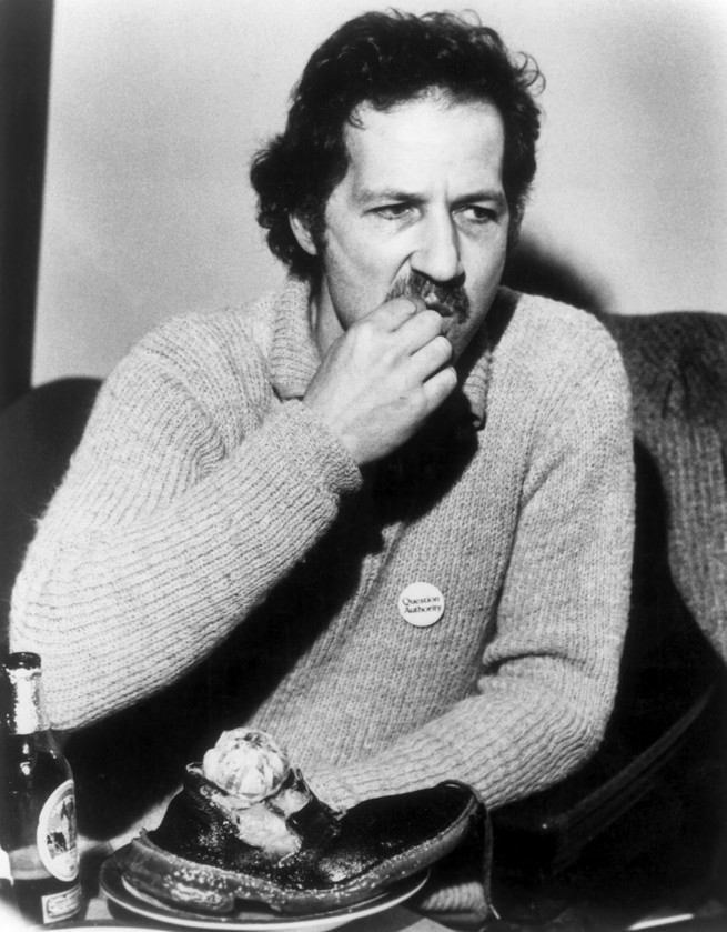 black and white photo of man with mustache chewing with part of shoe on table in front of him