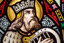 A stained-glass window of King David wearing a crown and playing a hand harp