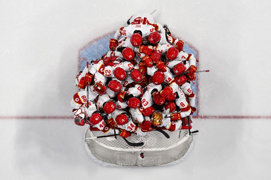 China's hockey team crushes together in a group hug in front of a goal, seen from above.