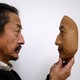 A man holds a realistic replica of a face.
