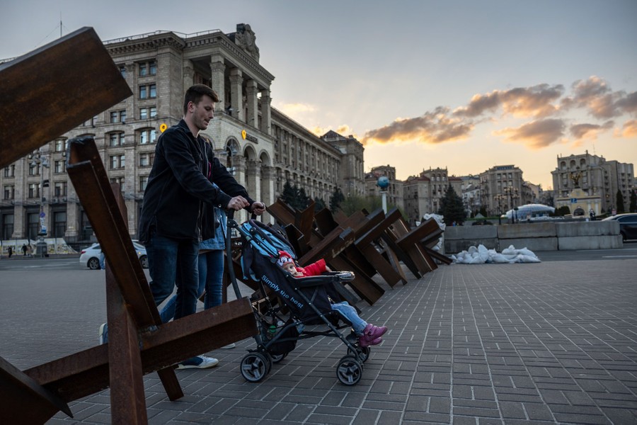 Two people push a baby stroller past tank barricades in a city square.