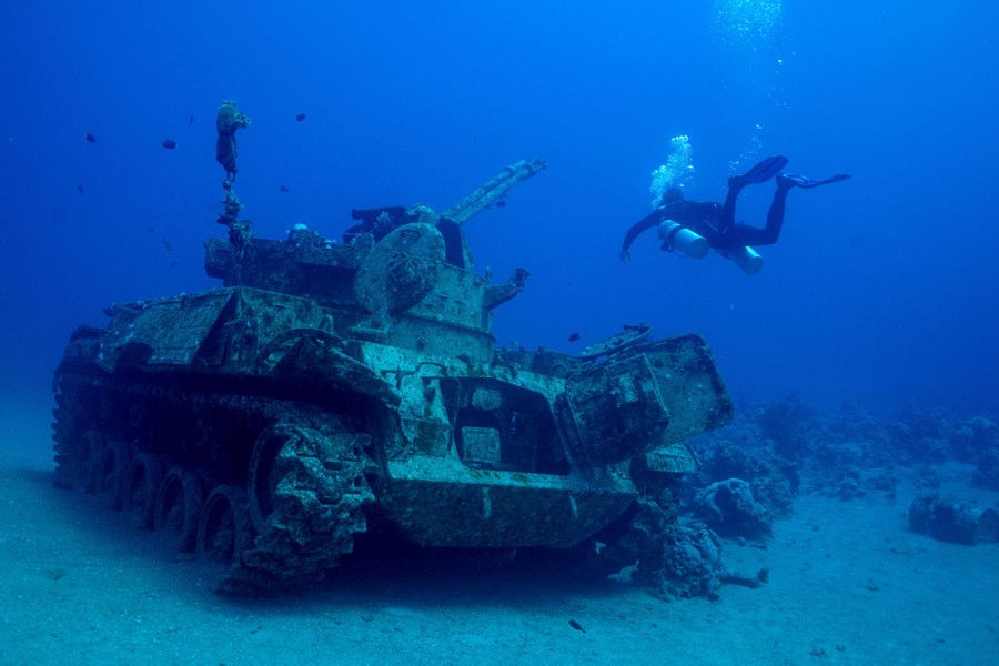 A scuba diver swims next to a submerged military tank.