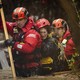 Two rescue workers help a person escape a flood, walking through waist-deep water.