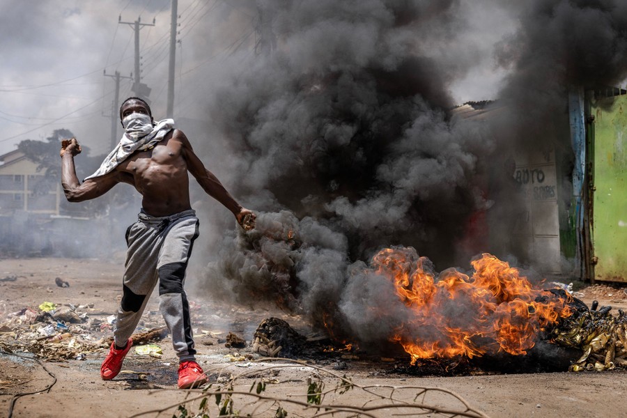 A protester throws a rock in a street beside a fire.