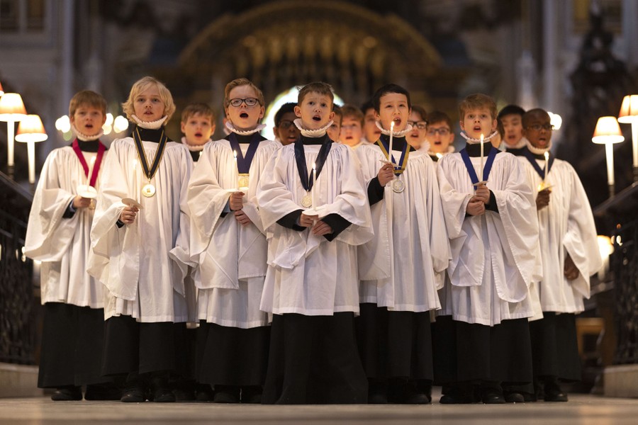 Children in choir robes sing in a cathedral while holding candles.