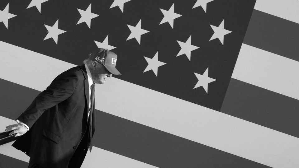 Black-and-white photograph of Donald Trump walking in front of the U.S. flag.