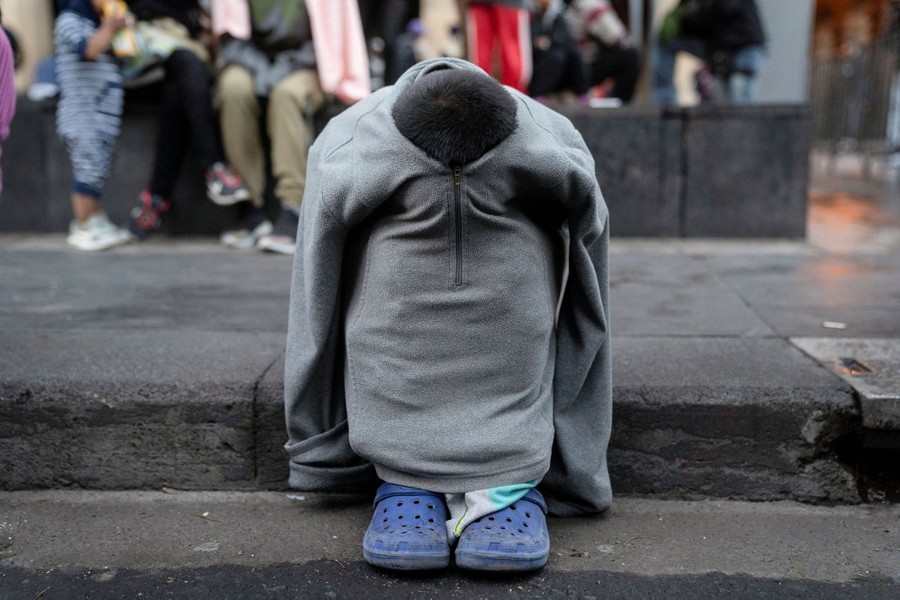 A child sits on an outdoor step, folded up inside their shirt, head and arms hidden inside.