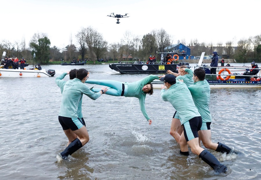 A team of rowers throws a teammate into a river.