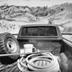 a photo of the rear of a pickup truck, its bed filled two buckets, a tire, and a hose, parked facing a mural of a mountain scene