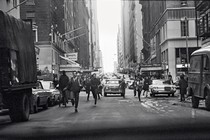 black-and-white photo of NYC street with people running alongside cars