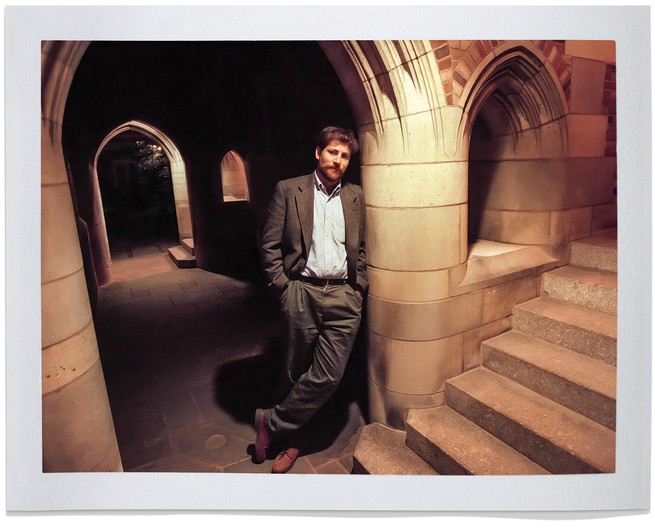 bearded man in suit leans against gothic pillar in dimly lit building near stairs up