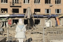 A woman in white stands before a shelled building