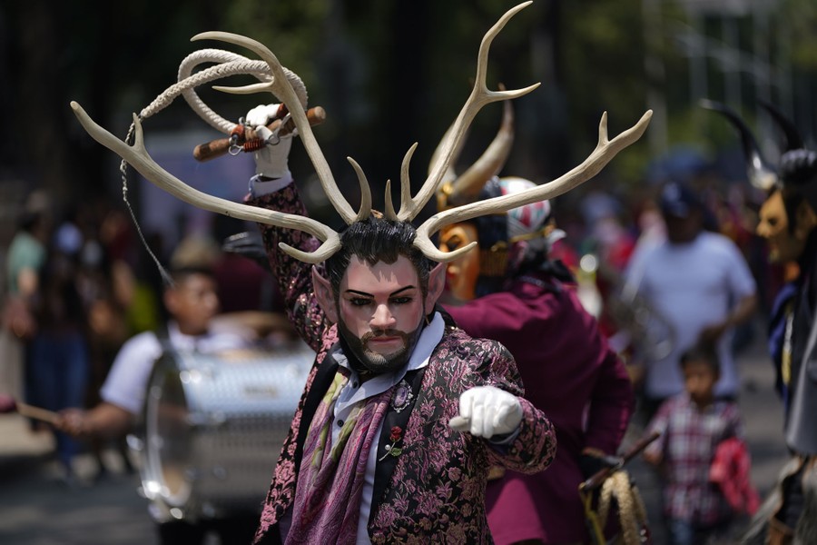 A costumed man wearing an antler headdress dances during a march.
