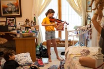 A young child playing violin in the center of a room where two other children and a dog are playing