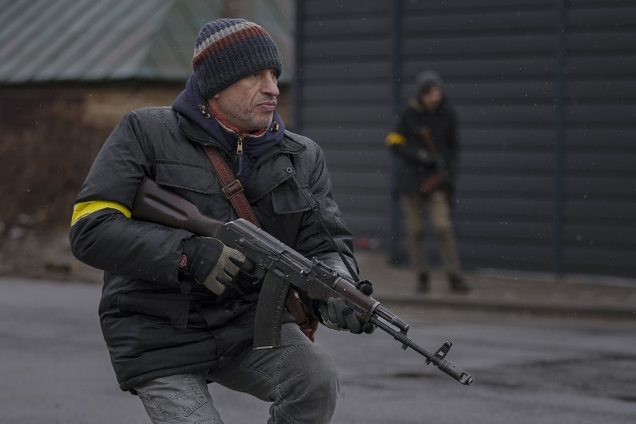 Two civilians carrying rifles guard a makeshift checkpoint on a city street.