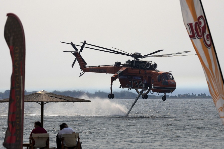 A firefighting helicopter flies low over water, filling up to make a drop.