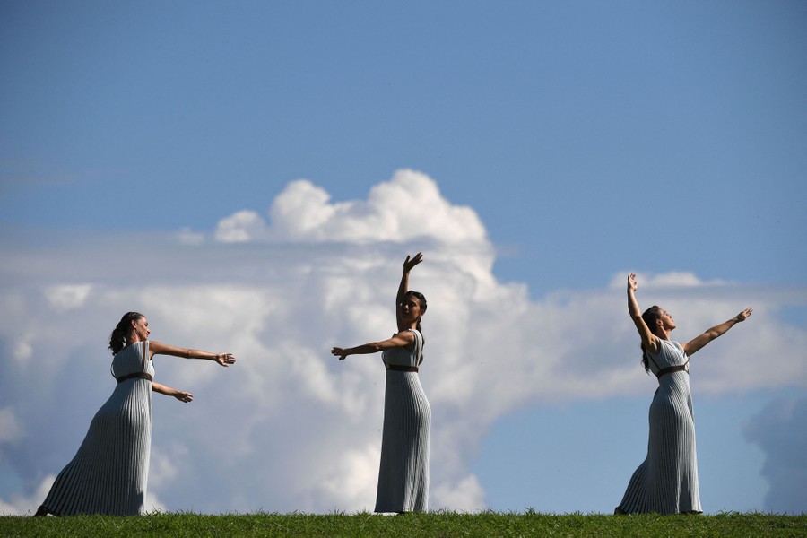 Three women wearing long gray dresses dance in an open field.