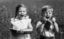 Two children in a field display extreme emotion while holding books.