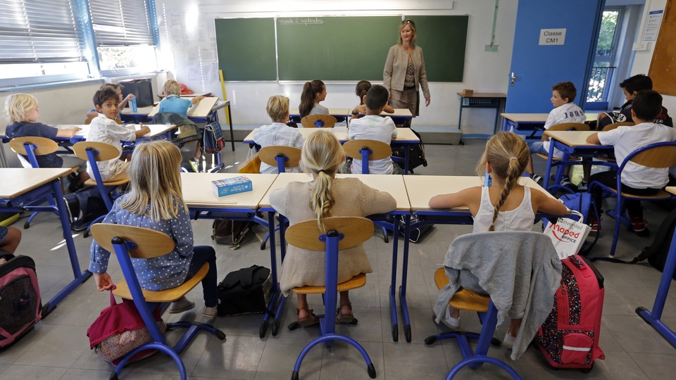 A teacher stands at the front of a classroom of students. 