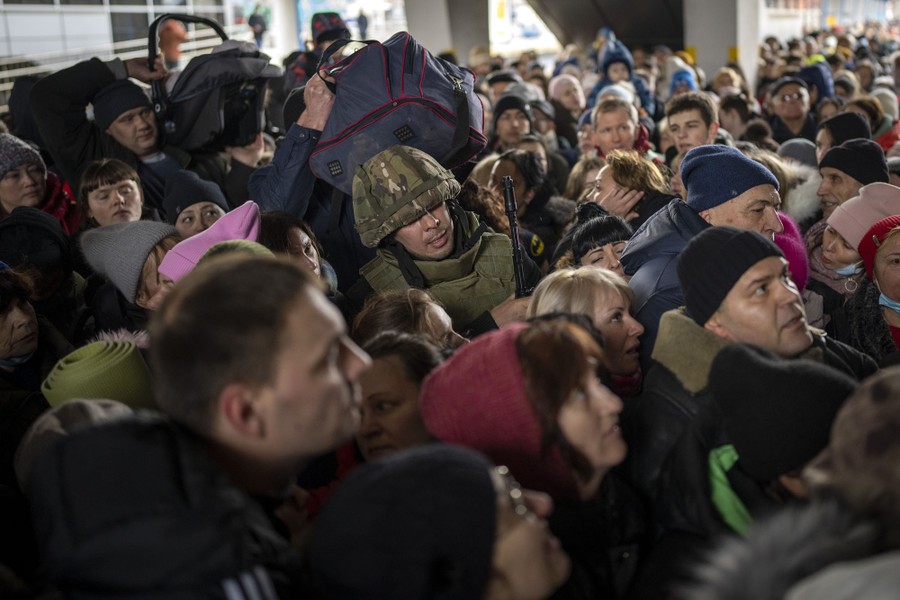 A weary-looking soldier stands in the middle of a large crowd of people trying to board a train.