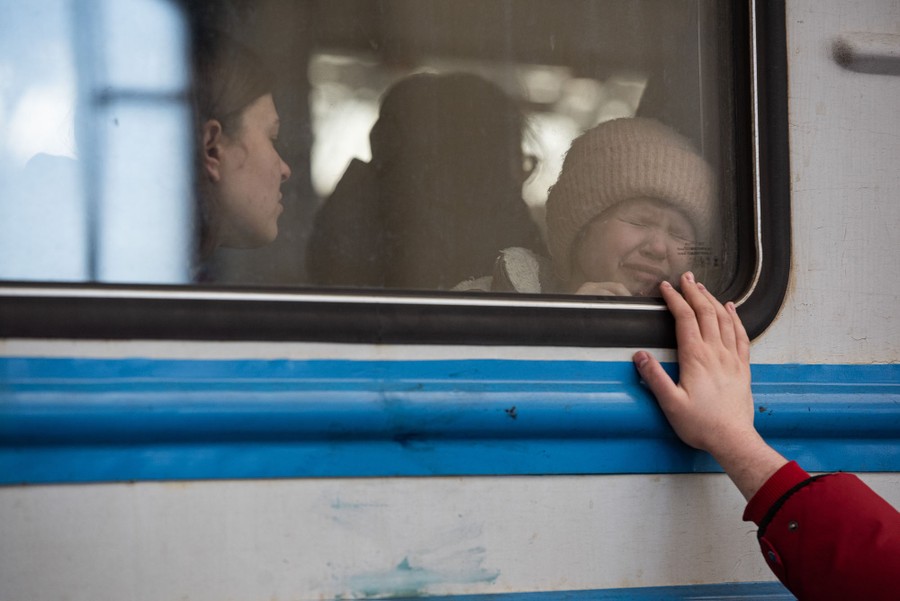 Uma jovem chora enquanto seu pai estende a mão até a janela do trem para se despedir.