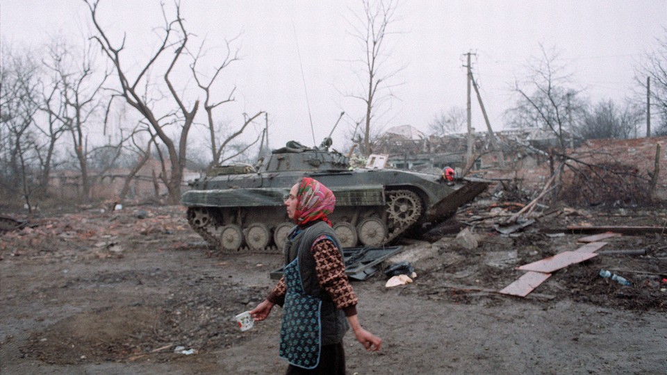 A women walks past a tank and ruins.