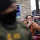 A woman hold a cellphone camera leans out from a car while an out of focus police officer stands in front of her.