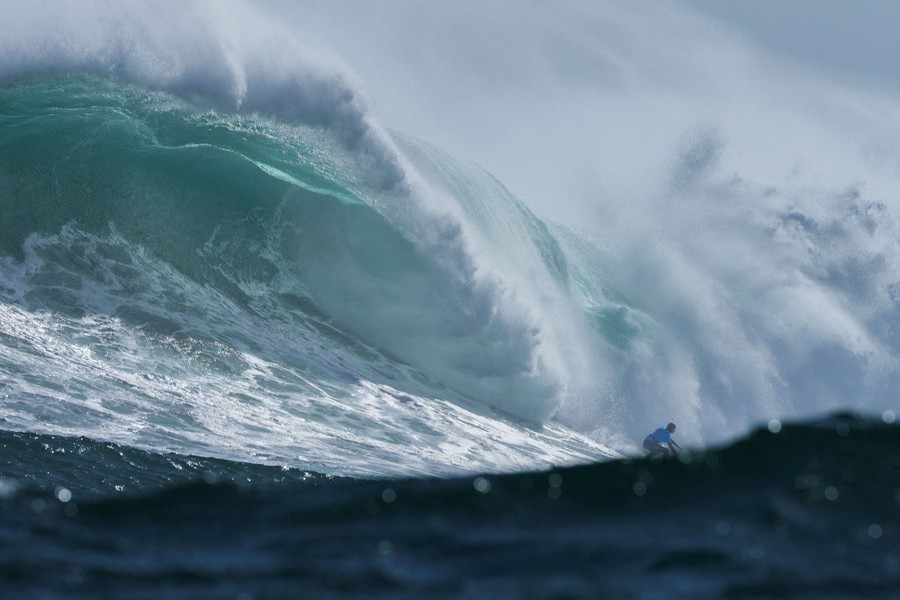 A surfer rides a huge crashing wave.