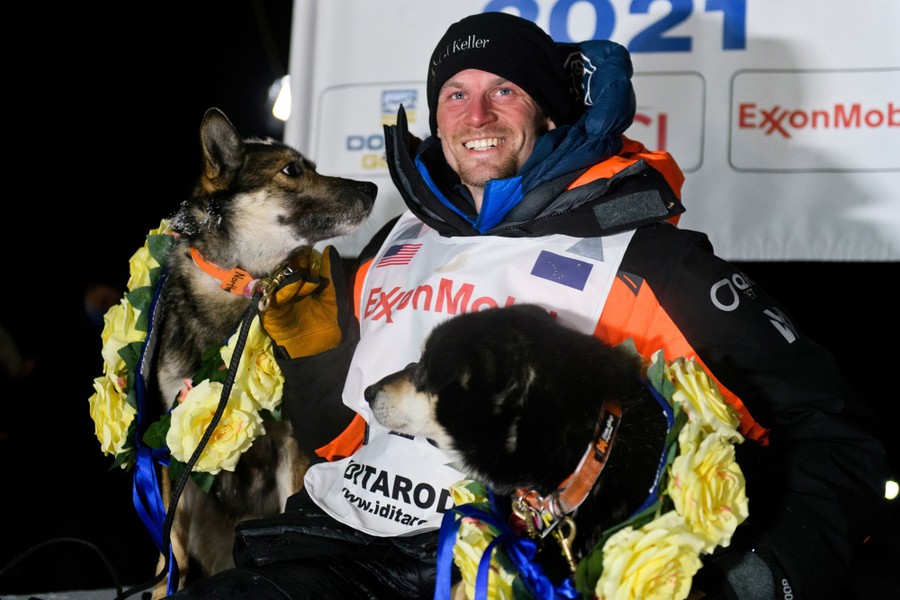 A musher poses for a photo with two of his dogs.
