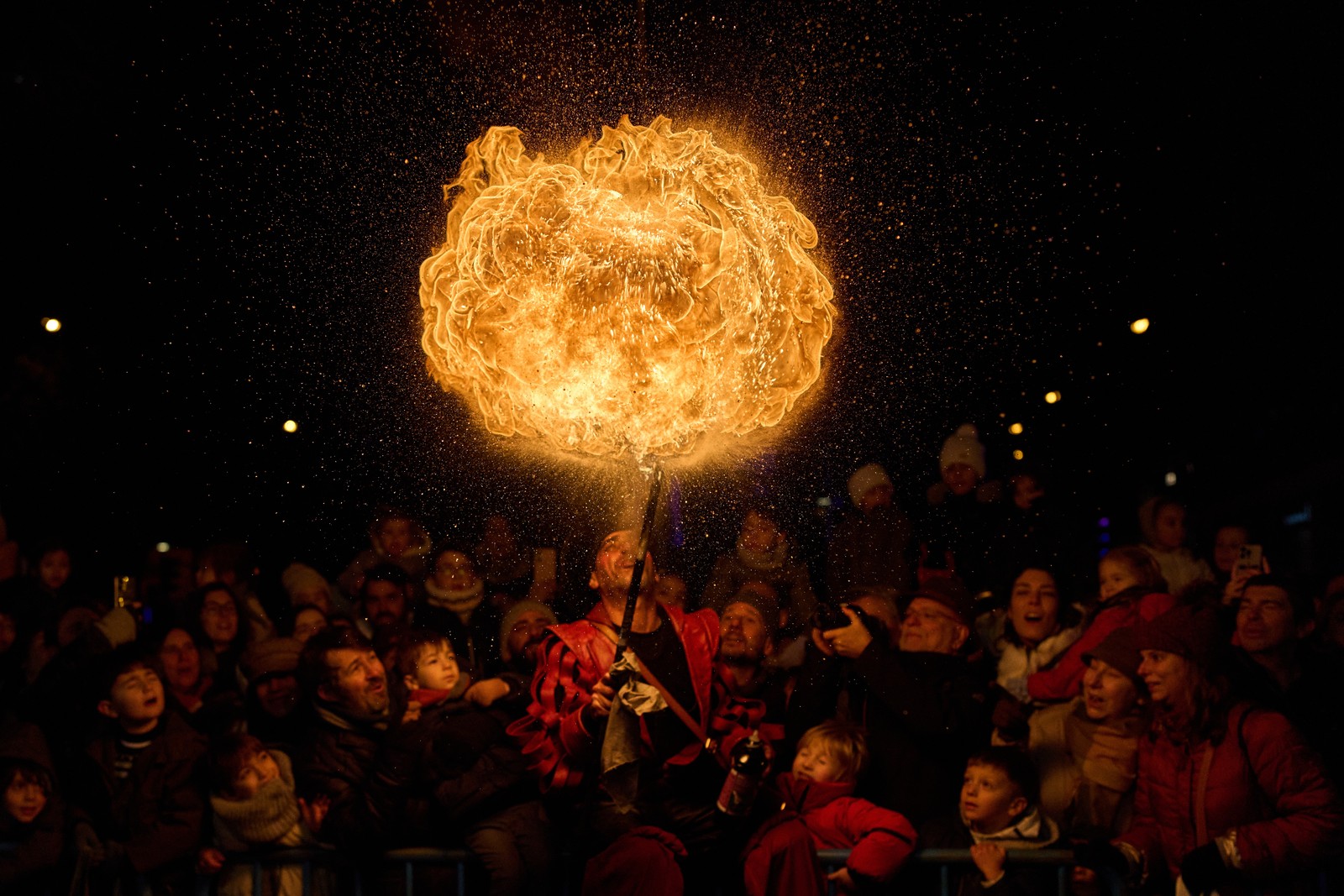A fire eater spits out flammable liquid, creating a ball of fire above a crowd of festival-goers.