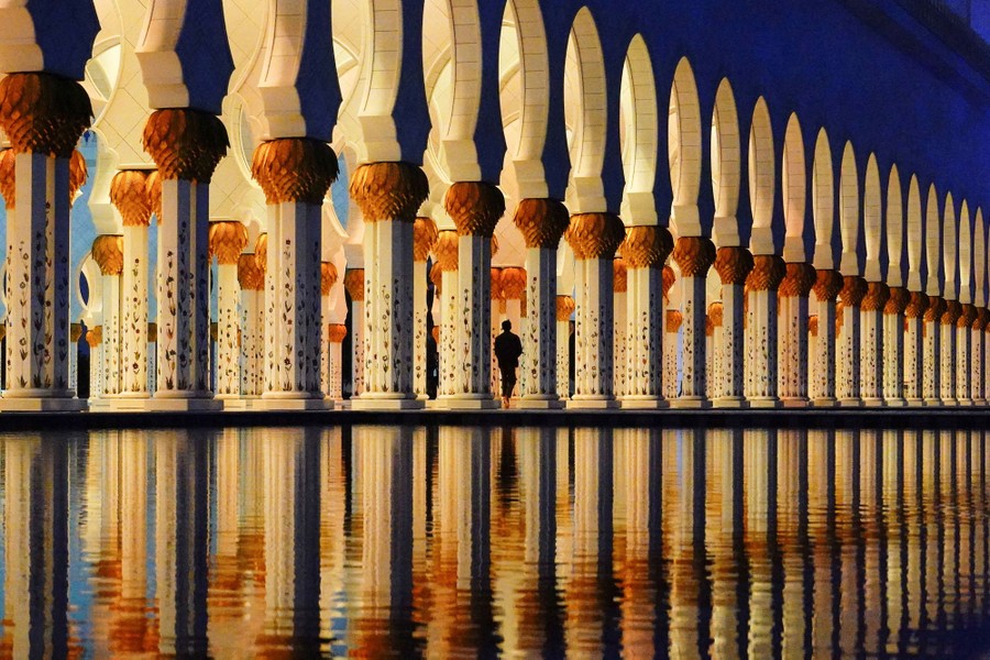 Ένα άτομο περπατά ανάμεσα σε διακοσμητικούς πυλώνες δίπλα σε μια αντανακλαστική λίμνη.