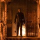 A masked Michael Myers stands on the porch of a burning house