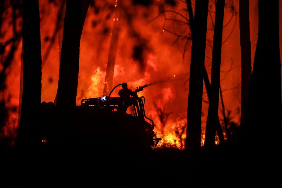 A firefighter sprays water from a truck toward a wildfire, at night.