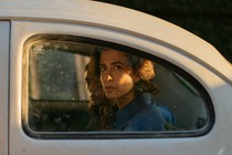 A woman looks out the back window of a car in a still from the film "I'm Still Here"