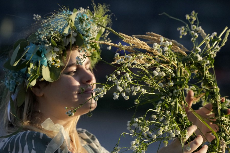 A woman wears and holds wreaths of flowers.
