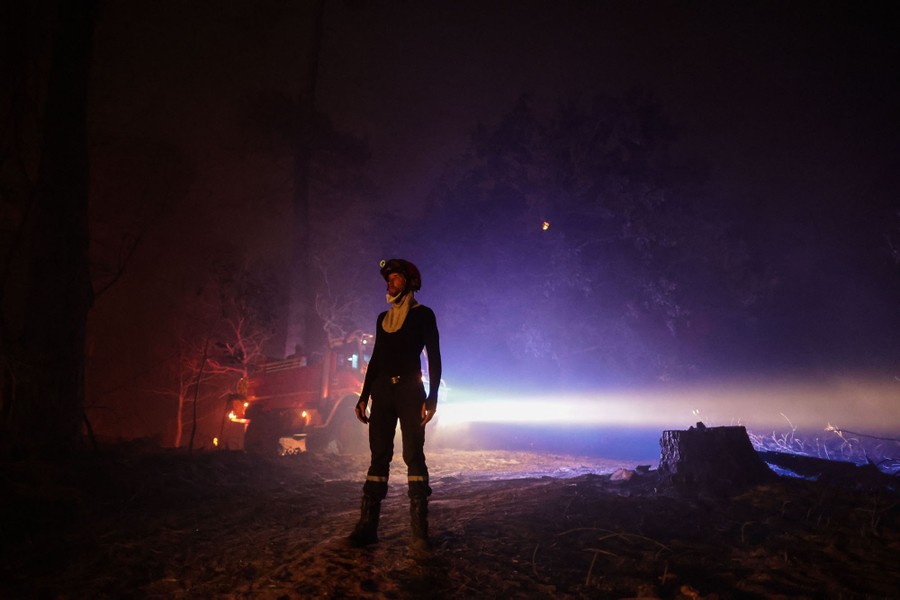 A firefighter stands in front of a firetruck at night, in a forest.