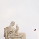 Marble statue of a woman holding a smaller marble statue in front of an American flag