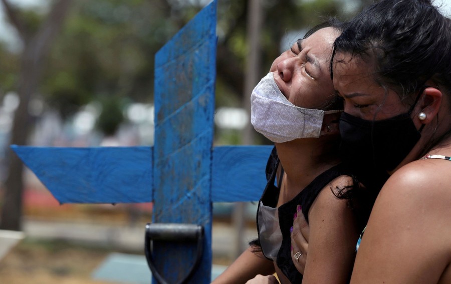 A woman supports her crying niece in a cemetery, during a burial.