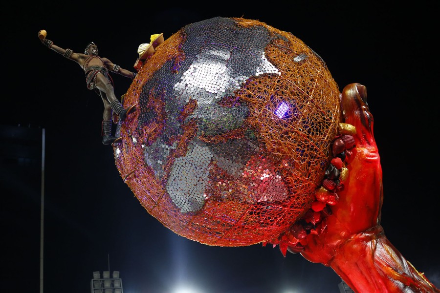 A dancer holds onto the side of a large globe, part of a parade float.