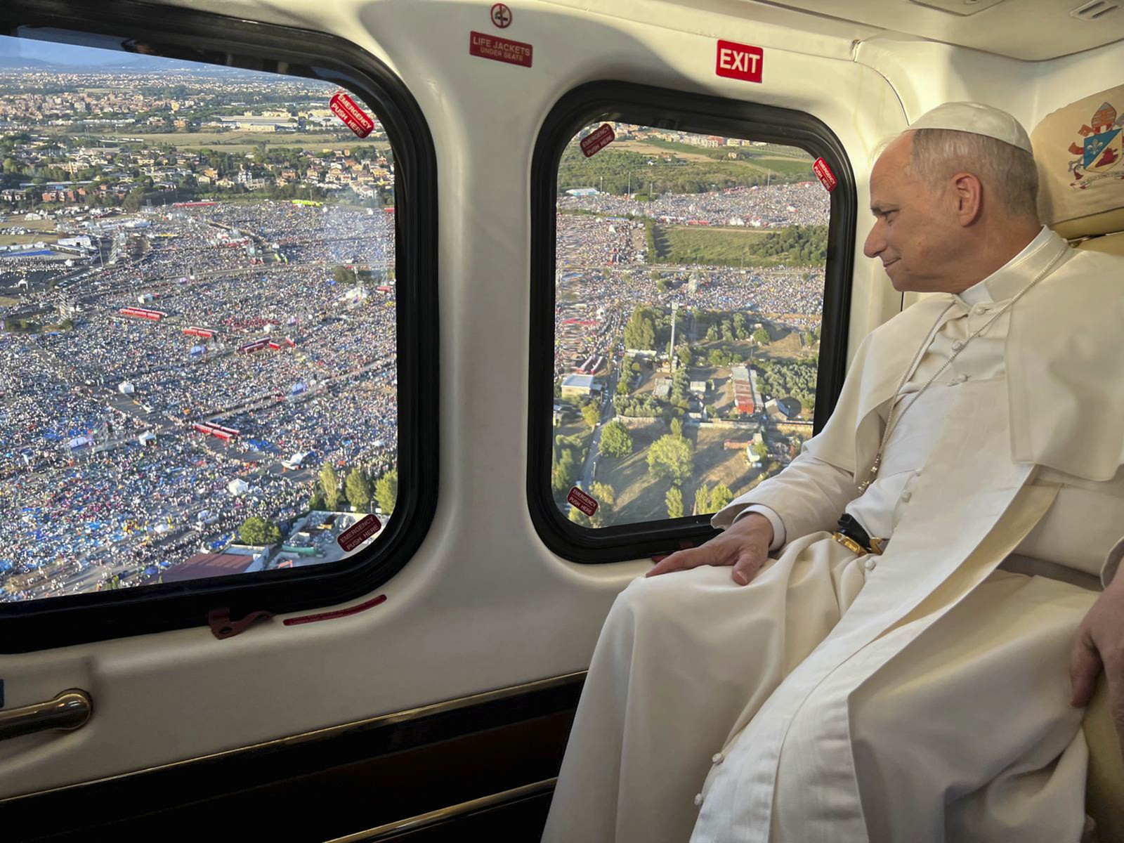 The Pope looks out the window of a helicopter over a crowded festival.