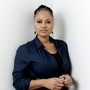 Ava DuVernay stands against a white background in a dark blue shirt