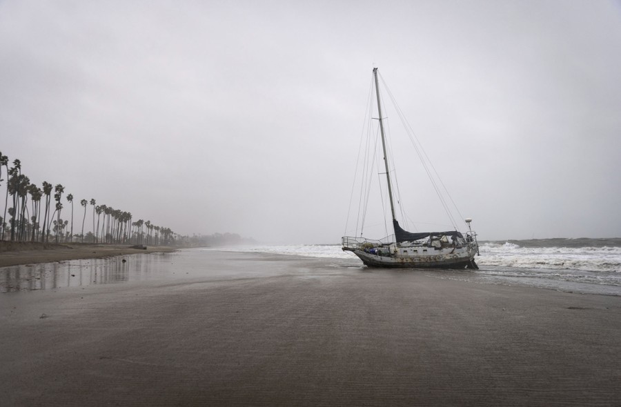 A sailboat sits grounded on a sandy beach during a storm.