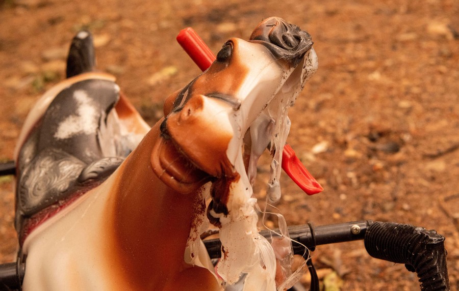 A melted rocking horse is seen near a burned house.